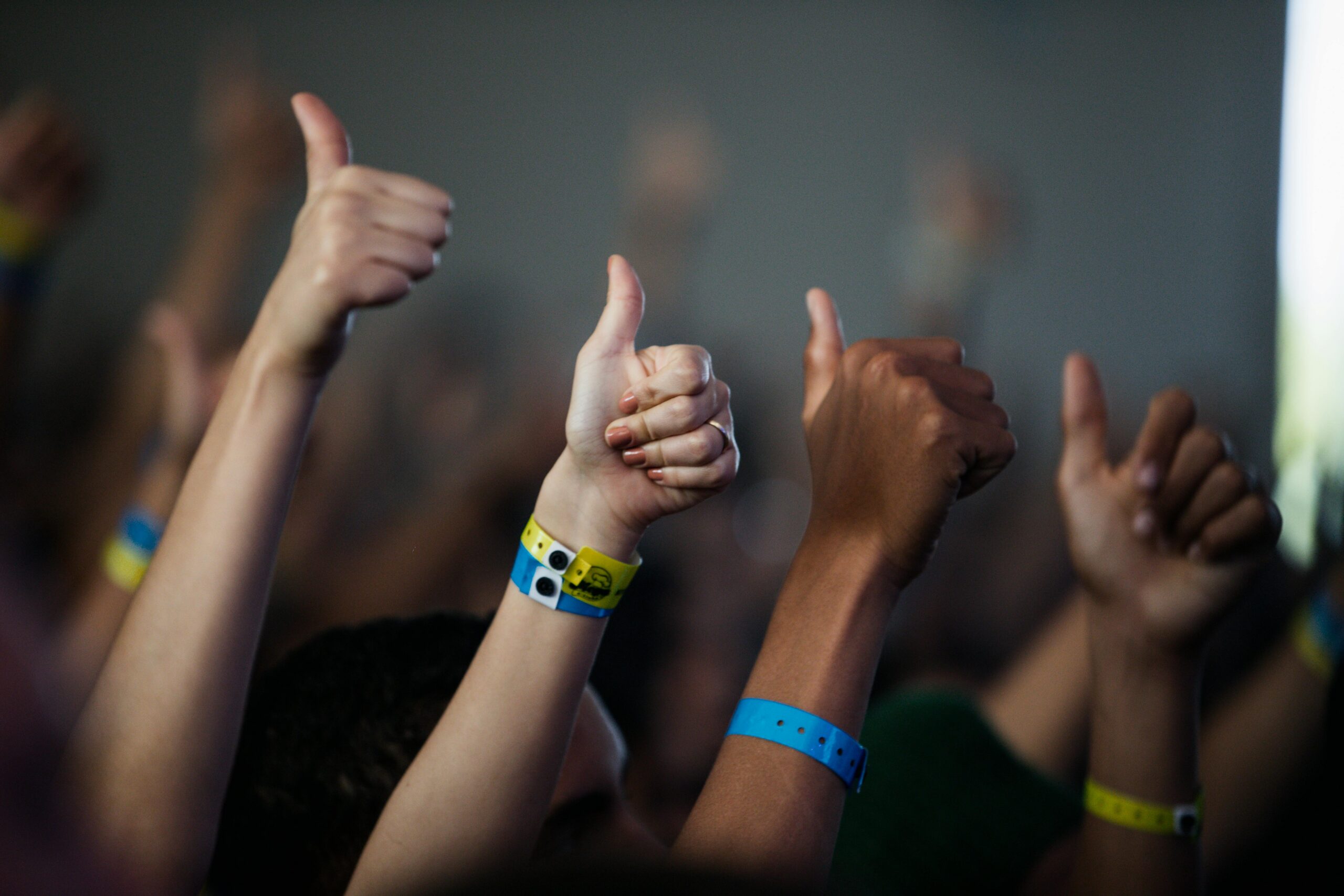 A group of diverse hands giving a thumbs up with colorful wristbands, showing unity and support.